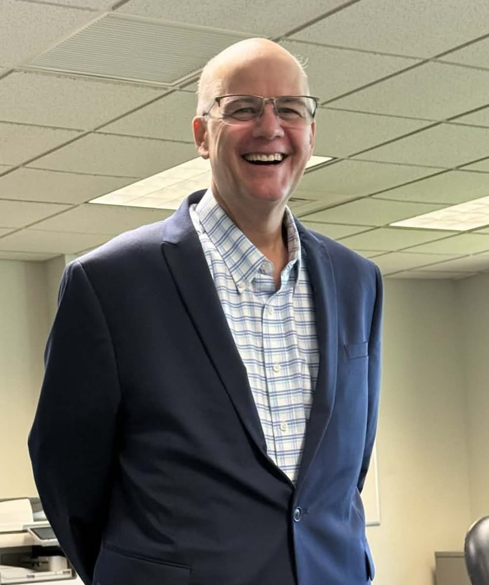 A man in a navy blazer, smiling.